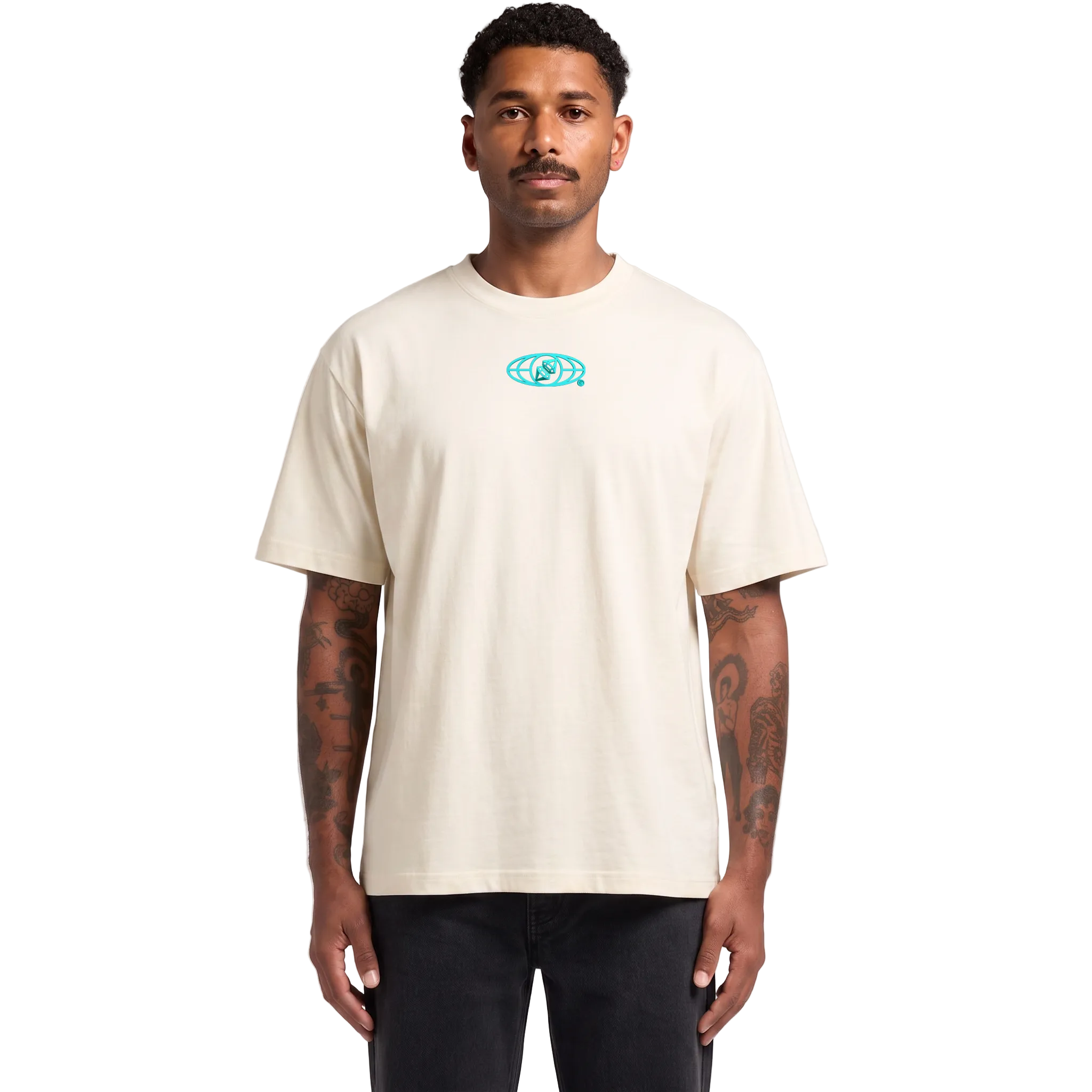 A man modeling a cream-colored crewneck t-shirt with a small turquoise graphic on the chest, paired with black pants, against a light gray studio background.