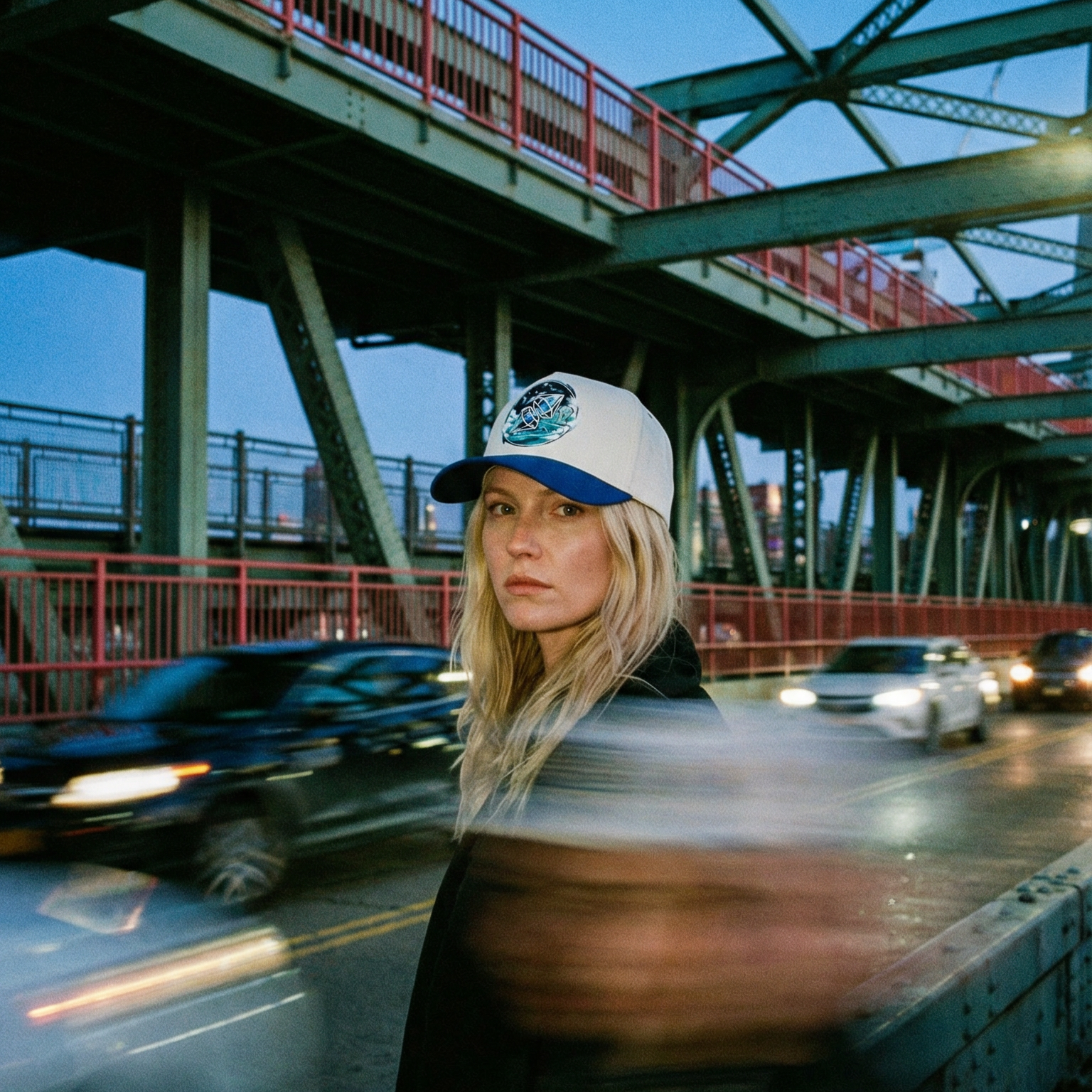 Woman wearing a cap on a bridge with cars passing by